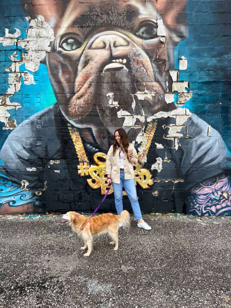 A girl and a dog standing in front of a dog mural painted on the side of a building.